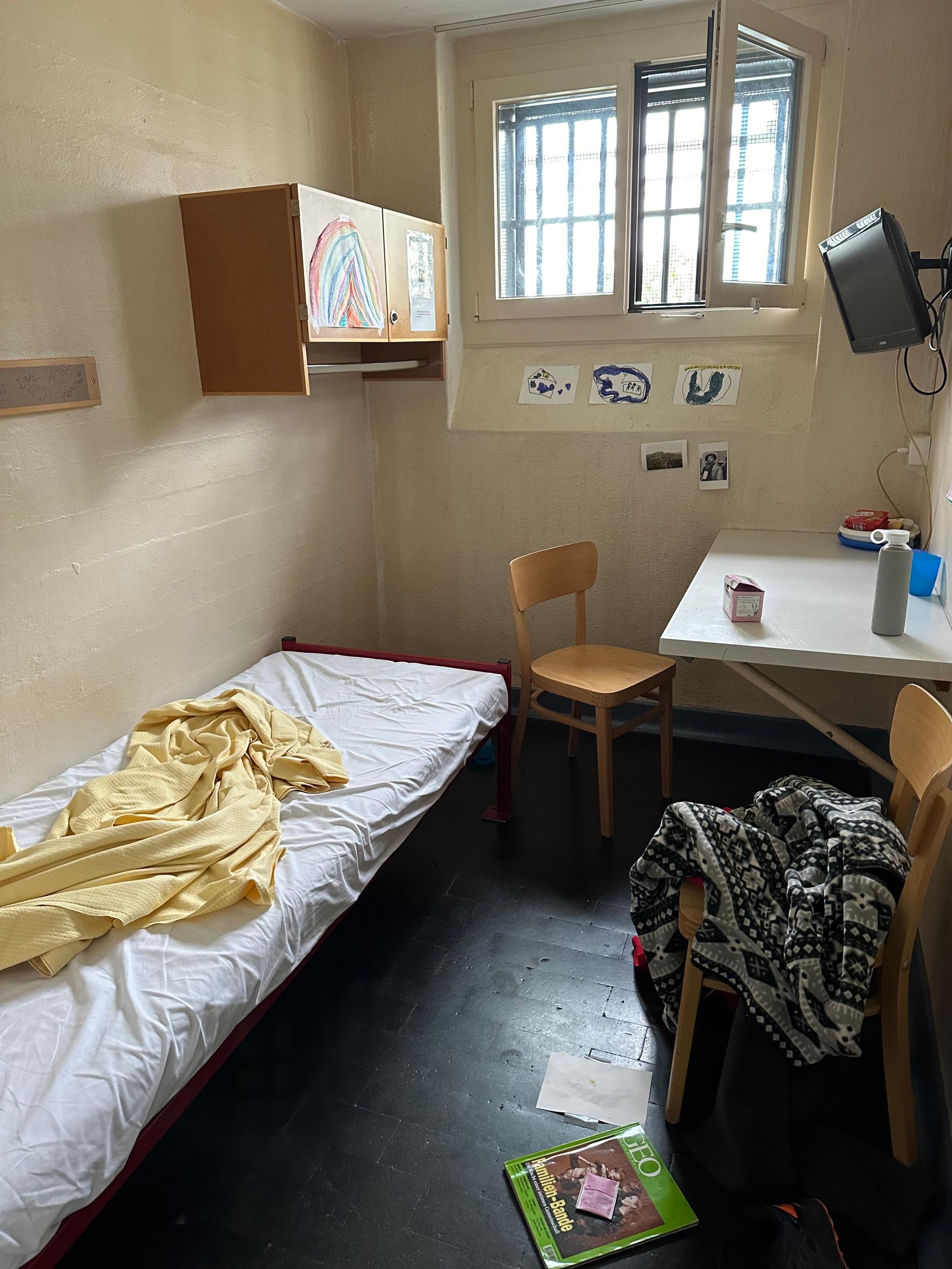 Die Einzelzelle hat ein Bett, Fenster, einen Tisch mit zwei Stühlen sowie einen Fernseher.