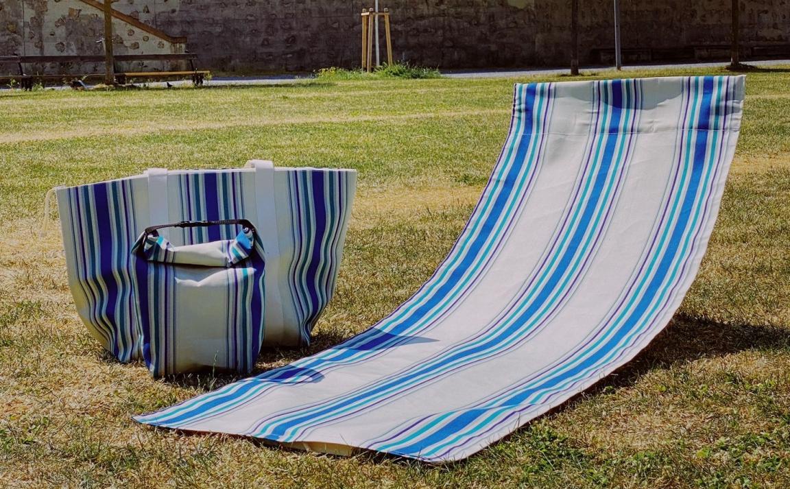 Tasche und Sonnenliege, blau-weiss gestreift liegt auf einer Wiese.