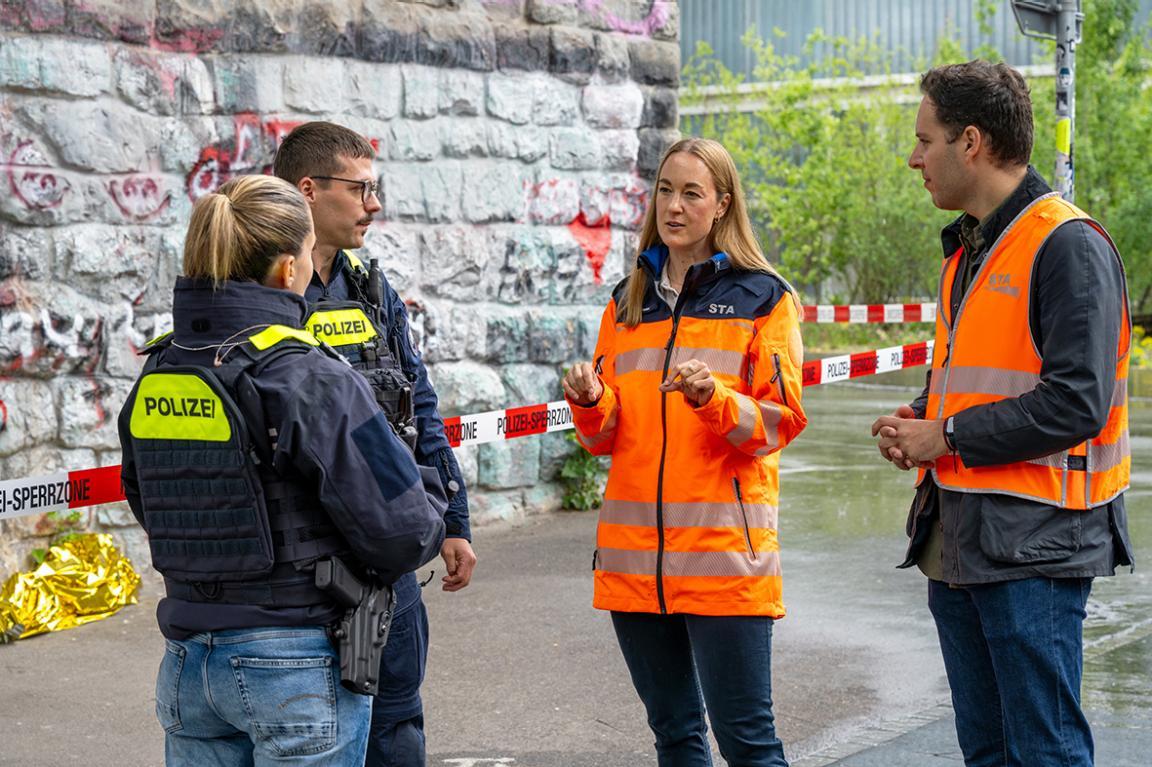 Zwei Mitarbeitende der Staatsanwaltschaft und zwei Polizisten stehen an einem abgesperrten Einsatzort und besprechen das weitere Vorgehen.