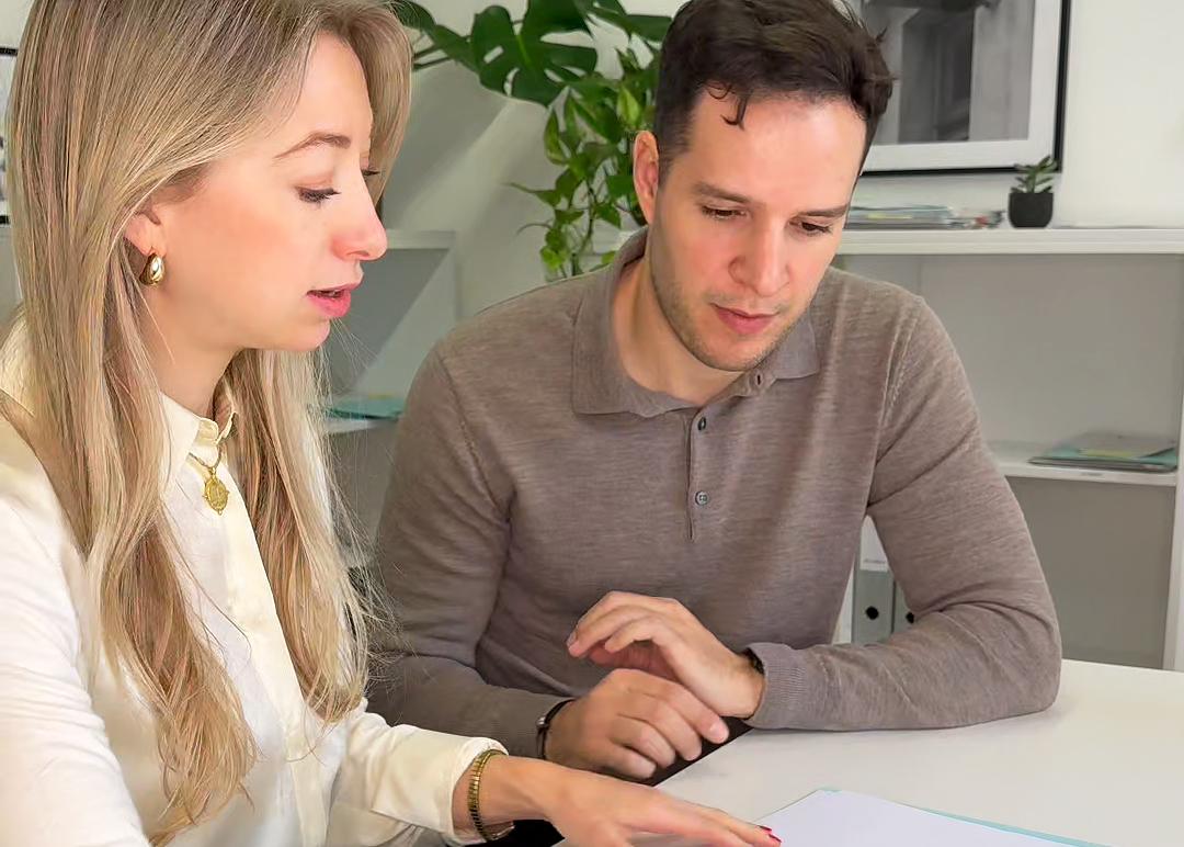 Eine Staatsanwältin und ein Assistenz-Staatsanwalt sitzen gemeinsam an einem Tisch und besprechen Unterlagen.