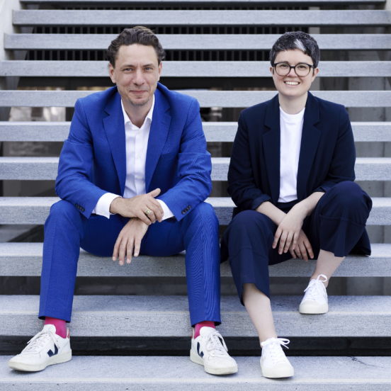 Foto, das die Co-Amtsleitenden Matthias Mazenauer und Andrea Schnell nebeneinander auf einer Treppe sitzend zeigt.