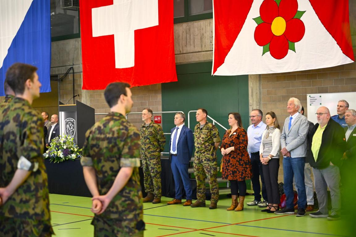 Regierungsrat Ernst Stocker steht mit anderen Behördenvertretern in der Turnhalle der Kaserne Birmensdorf an der Verabschiedung von Armeeangehörigen teil