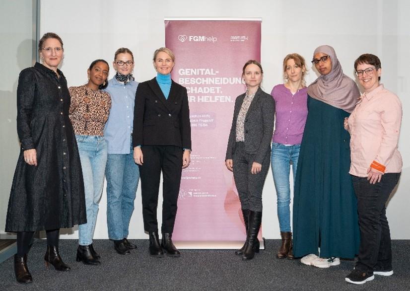 Eine Gruppe von acht Frauen steht vor einem Banner mit dem Logo «FGMhelp» und dem Text «GENITAL-BESCHNEIDUNG SCHADET. WIR HELFEN.», anlässlich des einjährigen Jubiläums.
