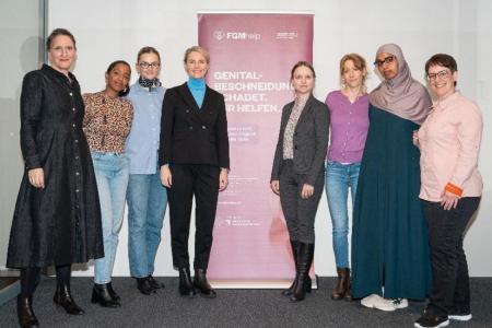 Eine Gruppe von acht Frauen steht vor einem Banner mit dem Logo «FGMhelp» und dem Text «GENITAL-BESCHNEIDUNG SCHADET. WIR HELFEN.», anlässlich des einjährigen Jubiläums.