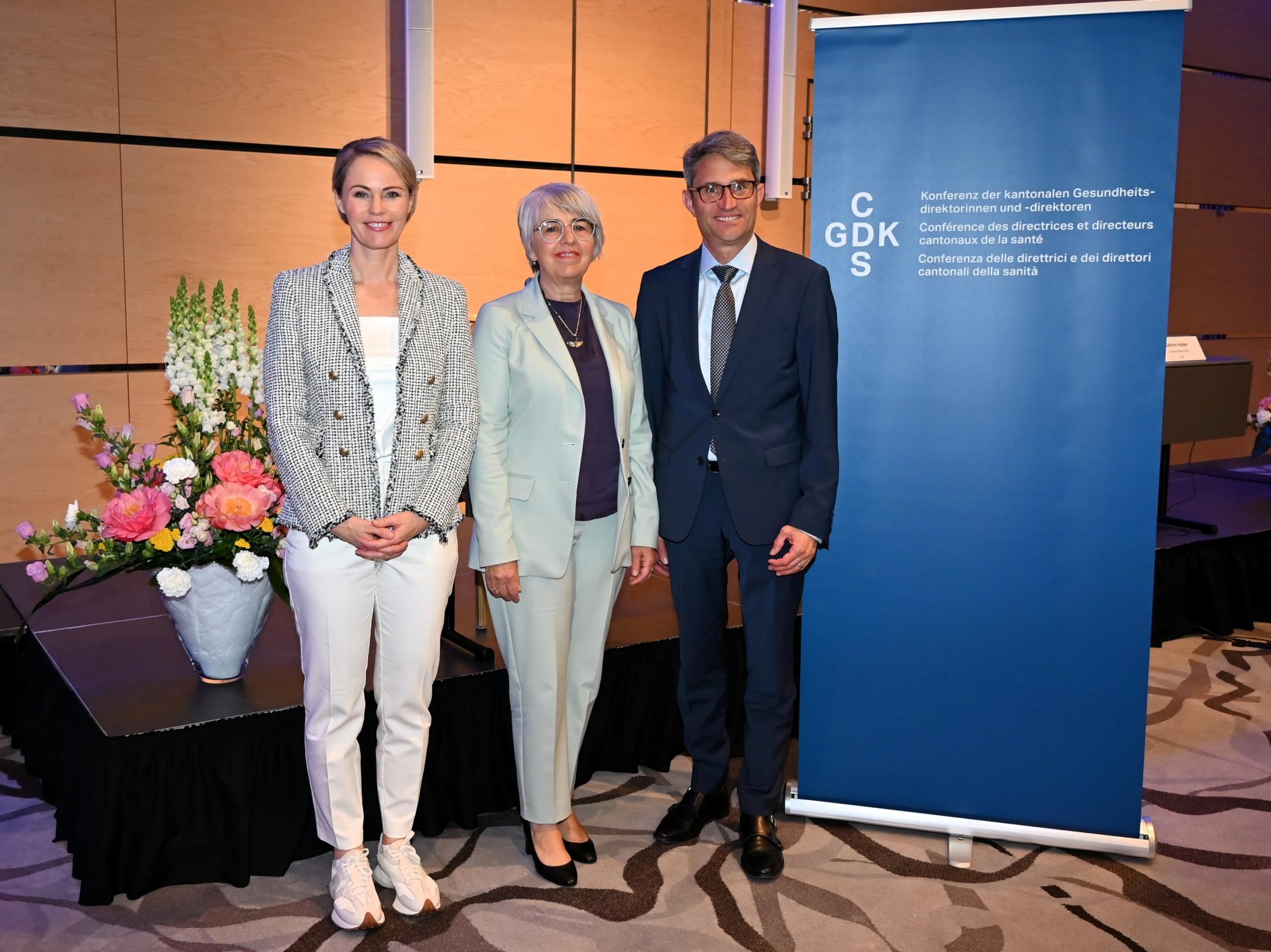 RR Rickli, BR Baume-Schneider und GDK-Präsident Engelberger posieren lächelnd vor einem blauen GDK-Banner bei der Jahrestagung.