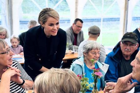 Regierungsrätin Rickli beugt sich lächelnd zu älteren Menschen an einem Tisch im Festzelt, es wird das Jubiläum des Altersheims gefeiert.