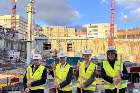 Regierungsrat Stocker, Spitalratspräsident Zemp, Regierungsrätin Rickli und CEO Jänicke in gelben Warnwesten und weissen Helmen mit «USZ»-Logo halten Spaten und stehen vor der grossen Baugrube des Universitätsspitals Zürich.