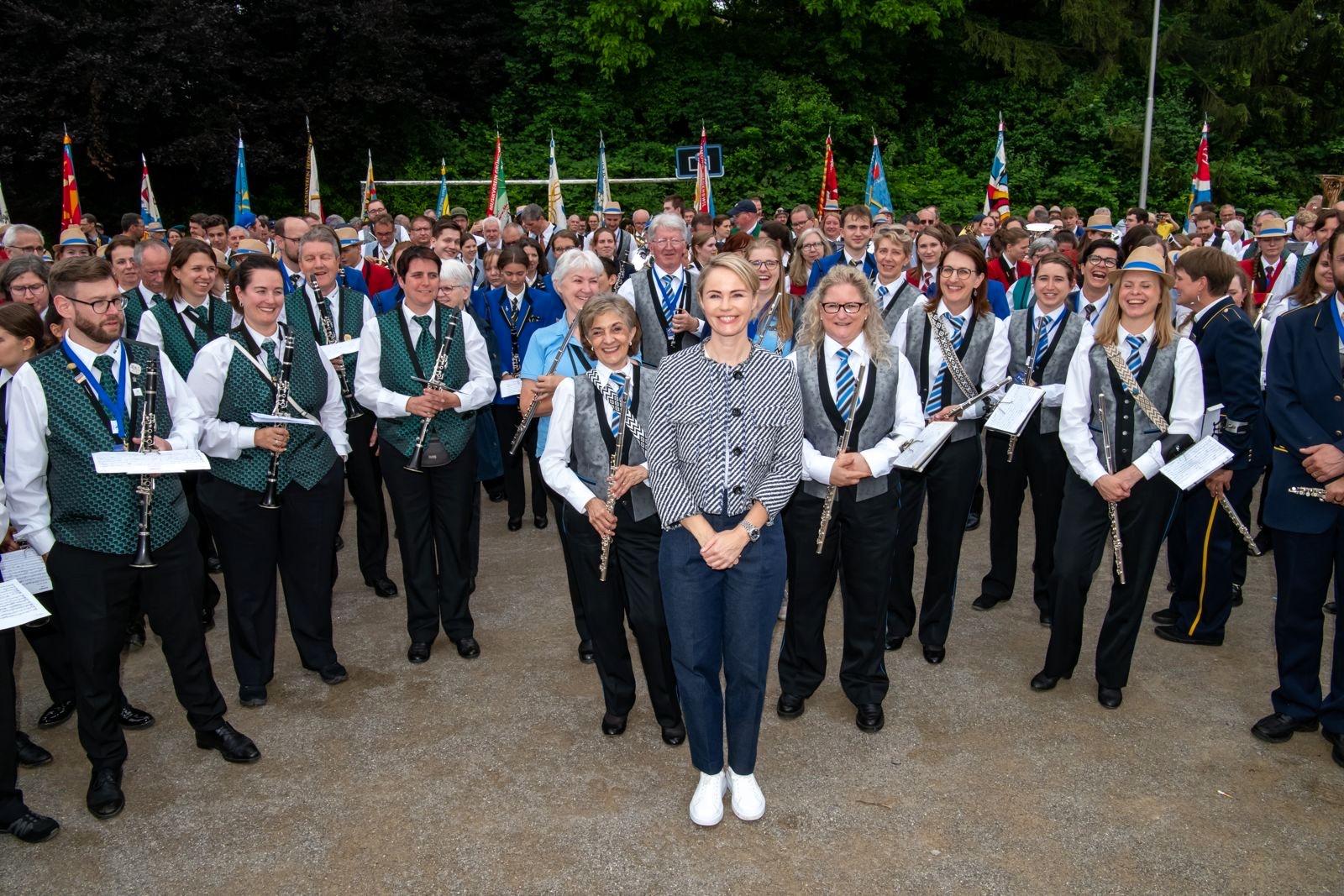 Regierungsrätin Rickli steht lächelnd zuvorderst inmitten einer grossen Gruppe Musikerinnen und Musiker des Kantonalmusikfests, die ihre Instrumente halten.