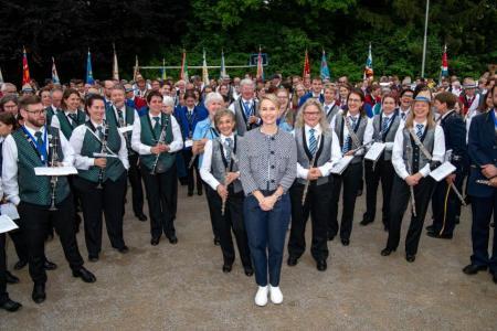 Regierungsrätin Rickli steht lächelnd zuvorderst inmitten einer grossen Gruppe Musikerinnen und Musiker des Kantonalmusikfests, die ihre Instrumente halten.