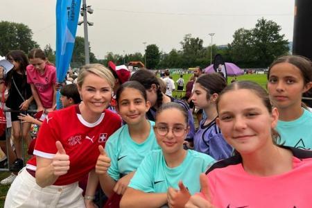 Eine lächelnde Regierungsrätin Rickli in rotem Schweizer Trikot und vier Mädchen zeigen Daumen hoch beim «Schüeli Dietikon», im Hintergrund Fussballplatz und viele weitere Jungen und Mädchen in Sportdresses..
