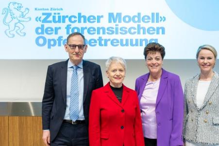 RR Mario Fehr, RR Jacqueline Fehr, RR Silvia Steiner und RR Natalie Rickli stehen lächelnd nebeneinander vor einer Präsentationsfolie zum Zürcher Modell der forensischen Opferbetreuung und blicken in die Kamera