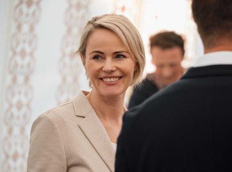 Regierungsrätin Rickli lächelt in beigem Blazer, zwei Personen neben ihr sind unscharf aufgenommen.