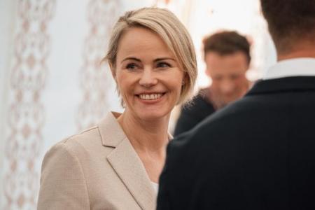 Regierungsrätin Rickli lächelt in beigem Blazer, zwei Personen neben ihr sind unscharf aufgenommen.