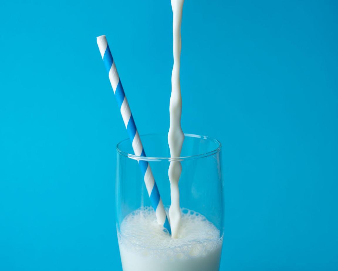 Blauer Hintergrund: In ein Glas wird Milch eingeschenkt