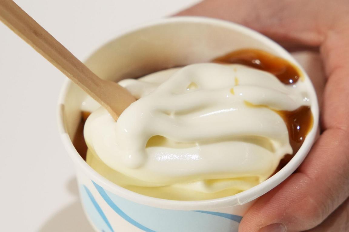 Becher mit Softeis und Löffel darin, gehalten von einer Hand.