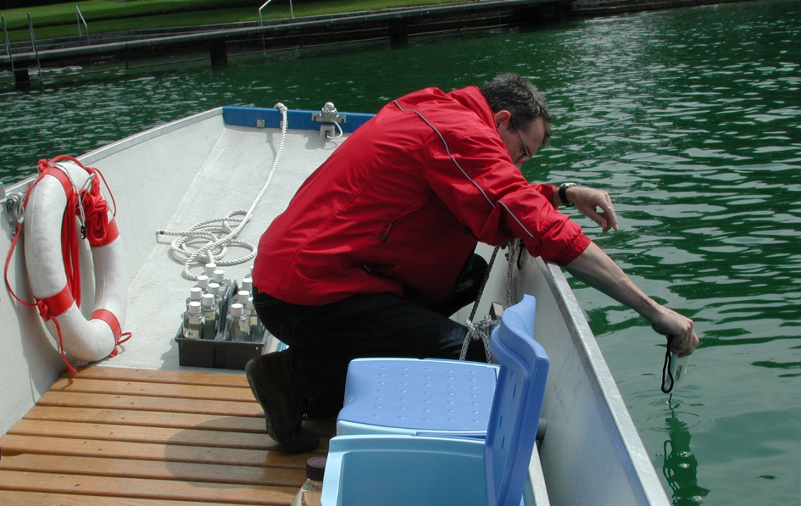 Ein Mann auf einem Boot hält ein Thermometer ins Wasser.