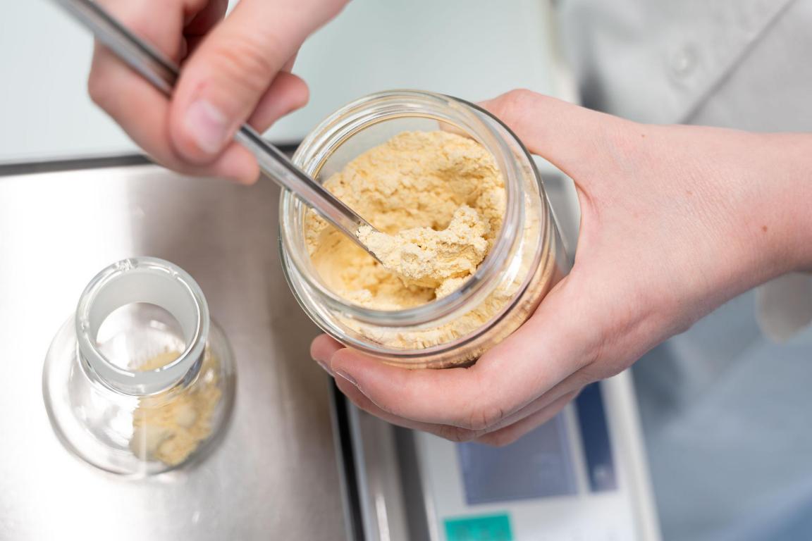 Kichererbsenmehl, das auf einer Analysenwaage in ein Laborglas eingewogen wird.