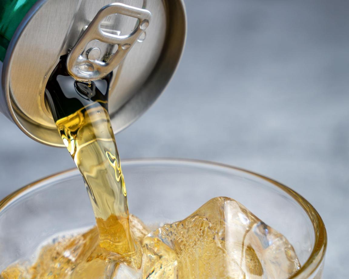 Ein Energydrink wird in ein Glas mit Eiswürfeln eingeschenkt.