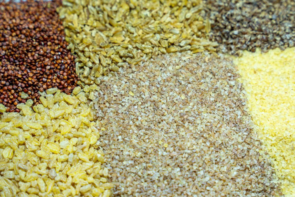 Nahaufnahme von unverpackten Getreide und Pseudogetreide, wie Freekeh, Quinoa, Bulgur und Couscous