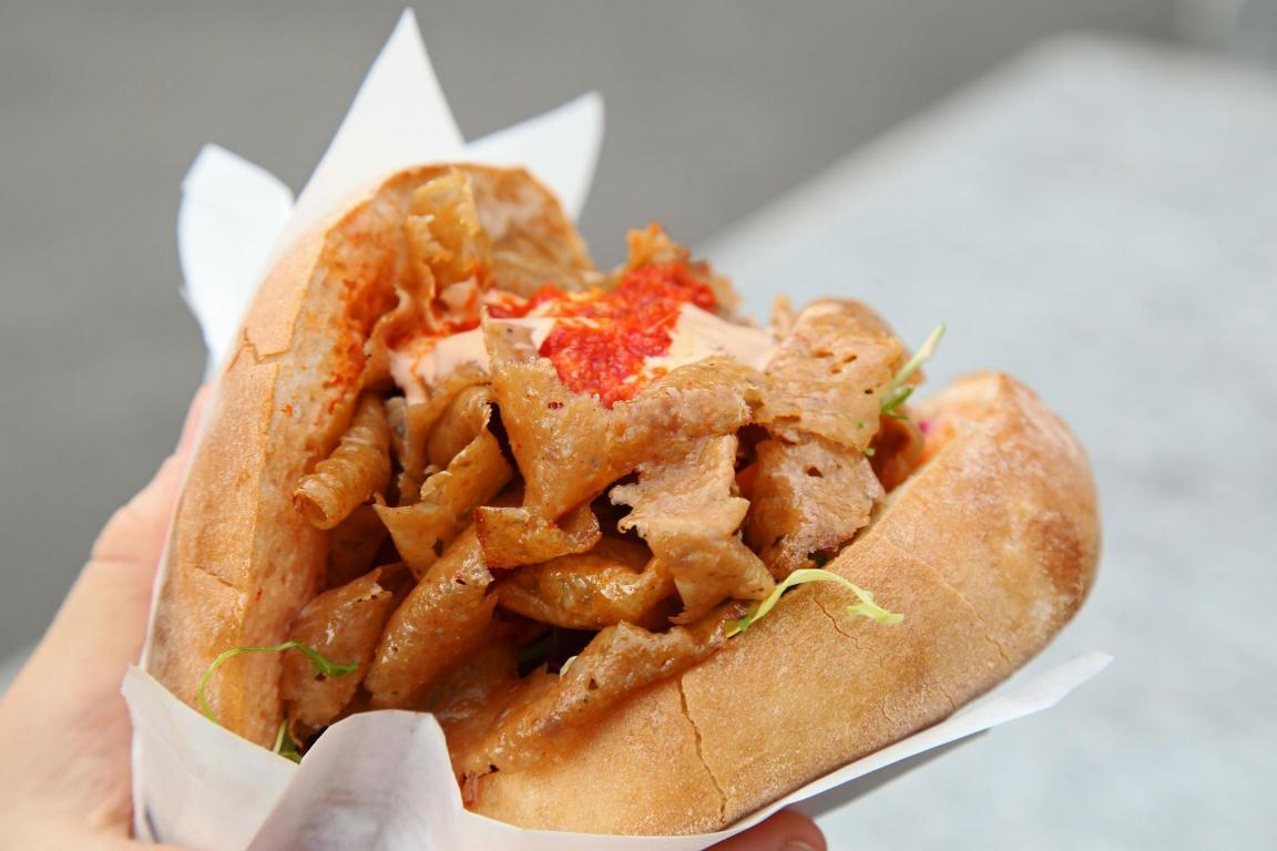 Eine Hand hält einen Döner Kebap im Taschenbrot gefüllt mit Kebabfleisch und mit roter Sauce.