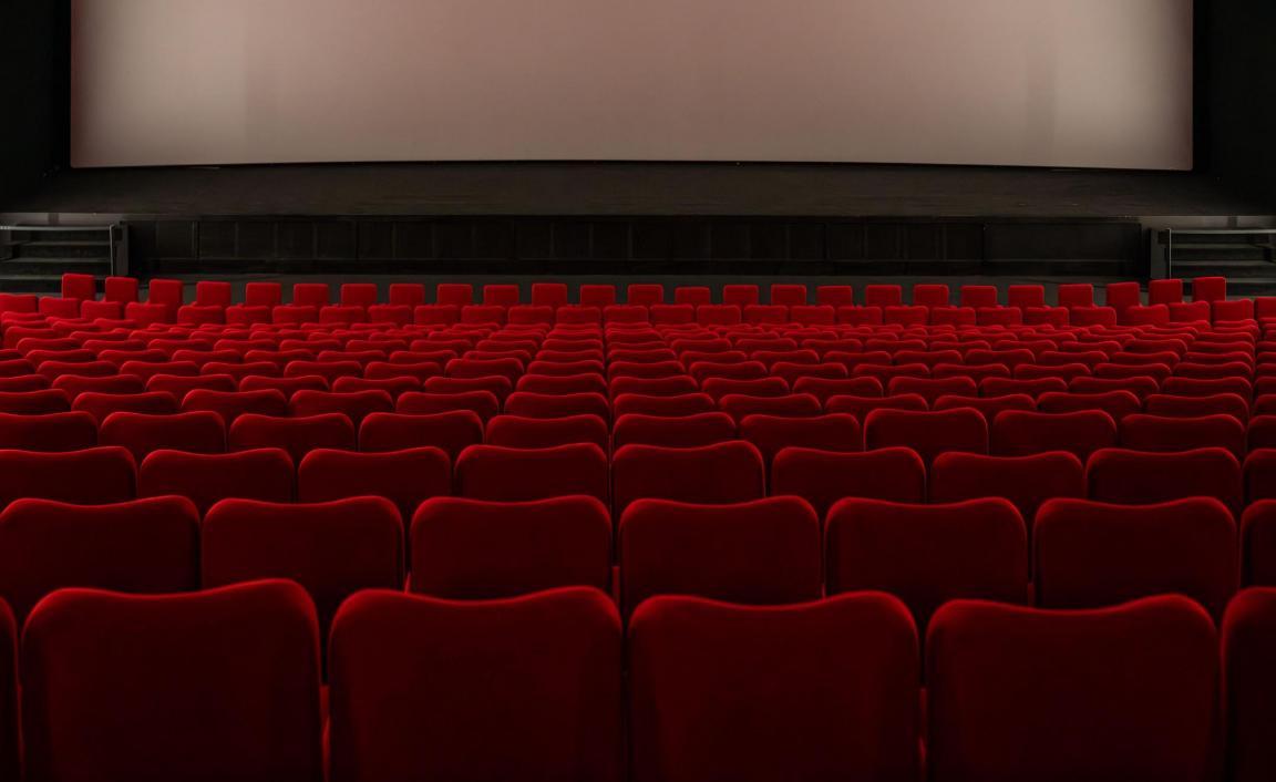 Im Kinosaal werden vor der Vorstellung die Vorhänge zur Seite gezogen. Die grosse Leinwand wird sichtbar. 