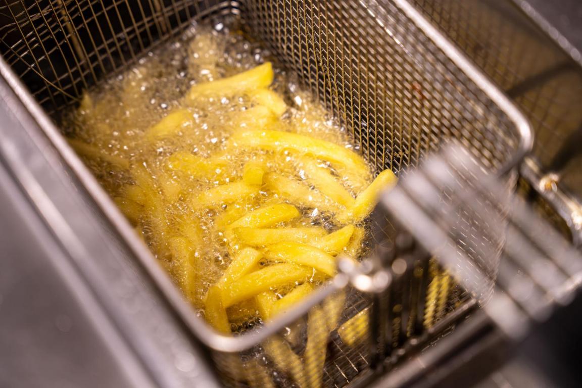 Pommes Frites in einem Frittierkorb werden in eine Fitteuse gehalten.