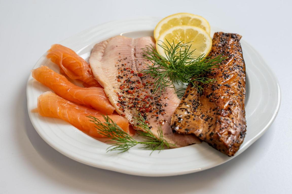 Drei verschiedene Arten Räucherfisch auf einem weissen Teller, dekoriert mit Dillzweigen und Zitronenscheiben.