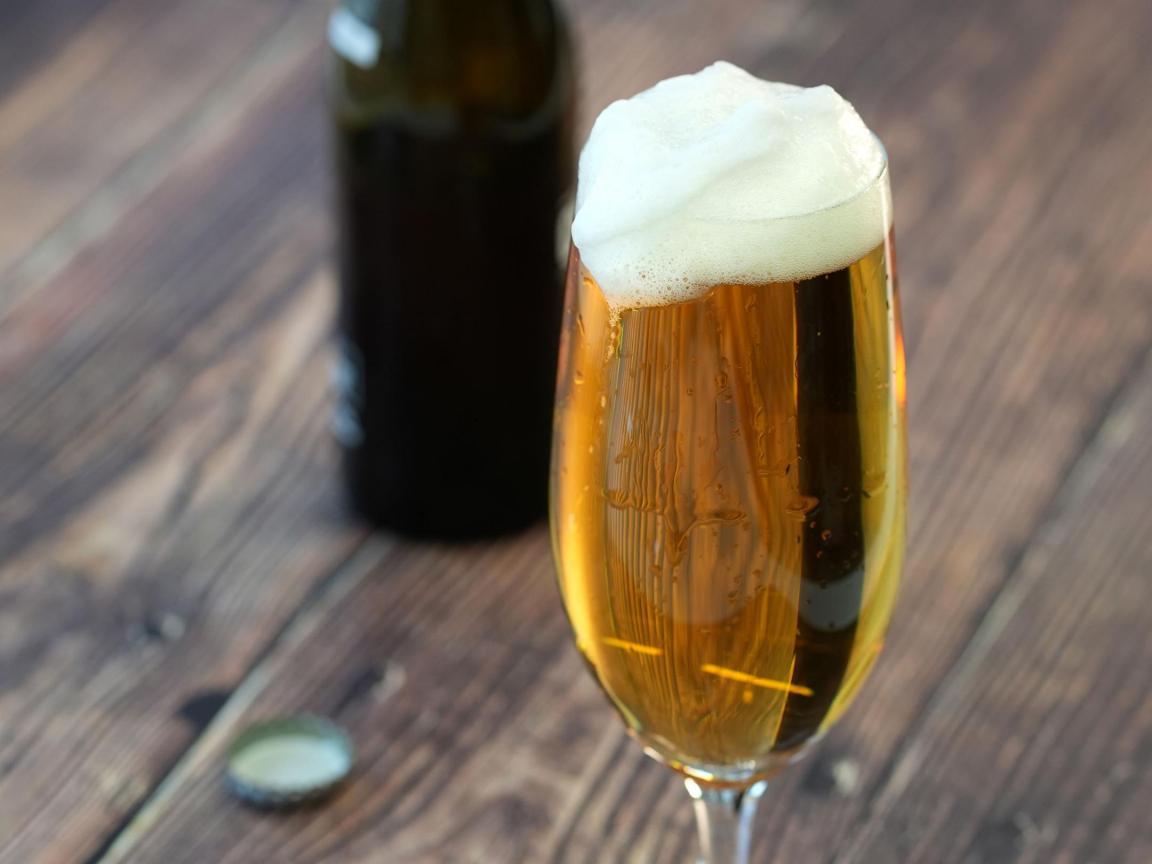 Gefülltes Bierglas mit Schaumkrone, im Hintergrund die geöffnete Flasche