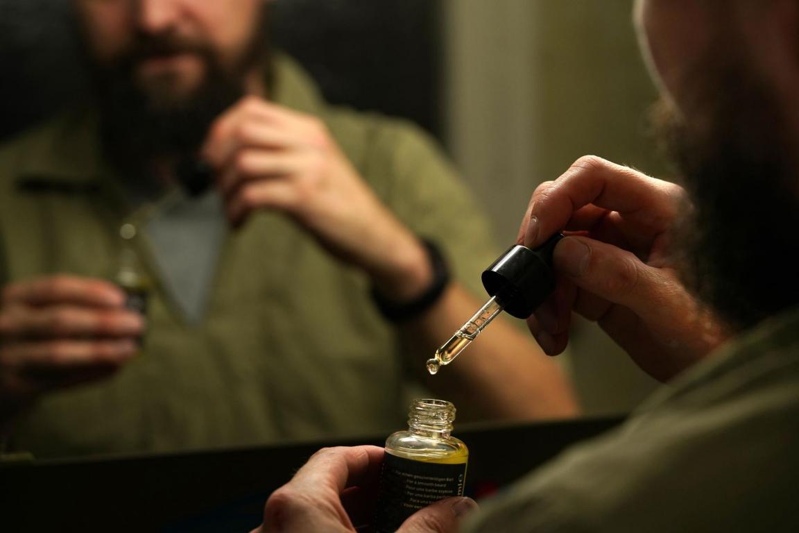 Mann vor Spiegel mit einem Bartölpflegeprodukt in der Hand
