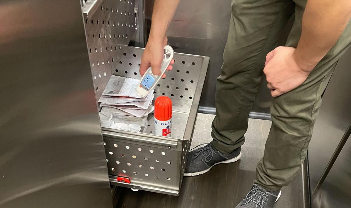 Ein Lebensmittelinspektor misst mit einem Thermometer die Temperatir in einer offenen Kühlschublade.