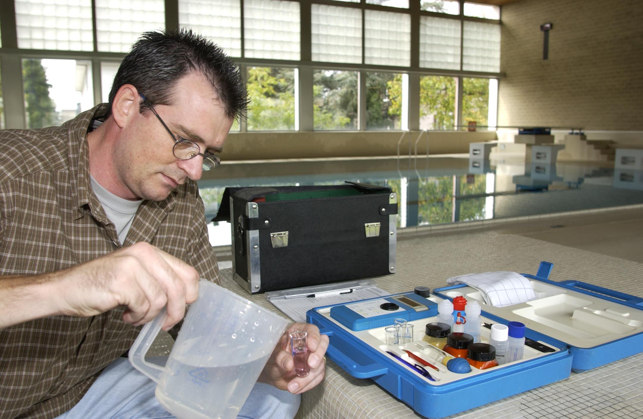 Ein Inspektor untersucht in einem Hallenbad das Badewasser.
