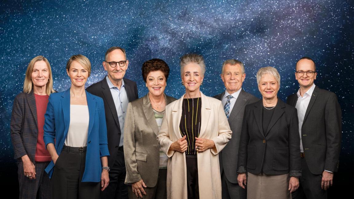 Die sieben Regierungsmitglieder und die Staatschreiberin vor der Kulisse des Weltalls