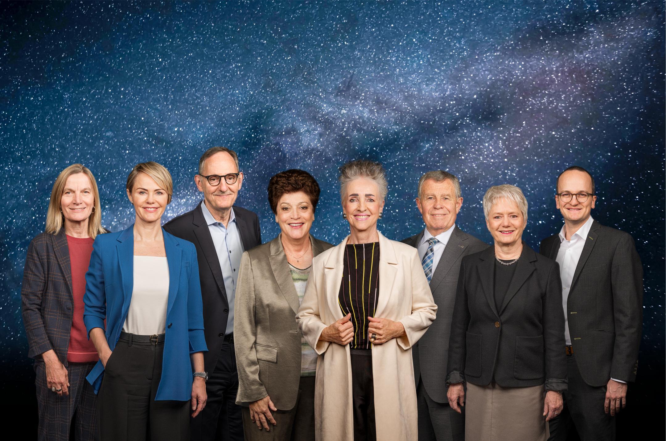 Die sieben Regierungsmitglieder und die Staatschreiberin vor der Kulisse des Weltalls