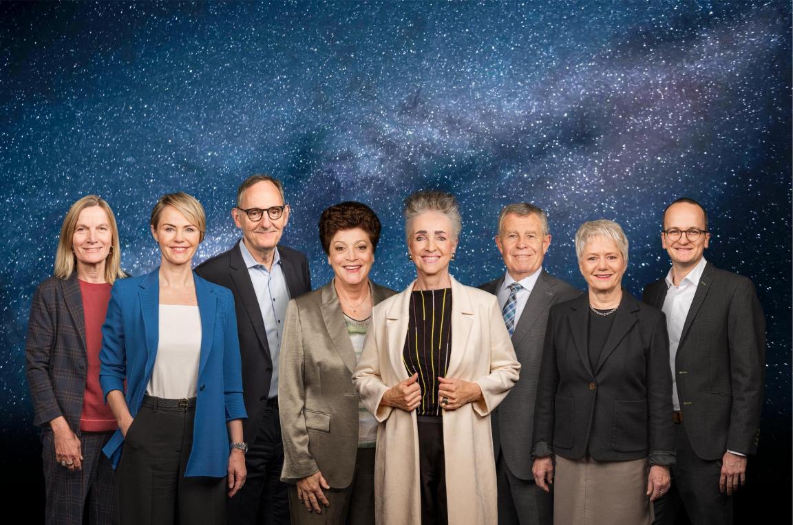 Die sieben Regierungsmitglieder und die Staatschreiberin vor der Kulisse des Weltalls