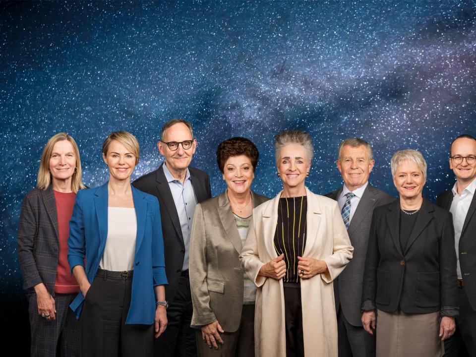Die sieben Regierungsmitglieder und die Staatschreiberin vor der Kulisse des Weltalls