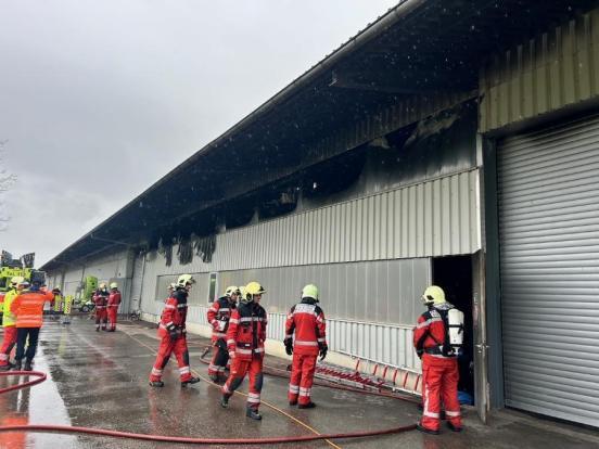 Mehrere Feuerwehrleute vor der beschädigten Lagerhalle