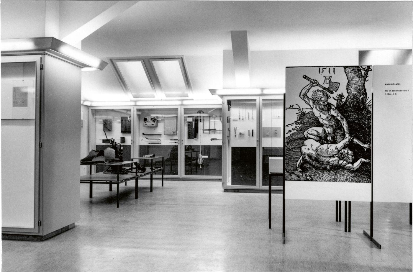 Schwarz-Weiss-Fotografie aus dem Kriminalmuseum nach dessen Öffnung für die Öffentlichkeit im Jahr 1958.. Sichtbar sind diverse Vitrinen mit Exponaten aus Kriminalfällen.