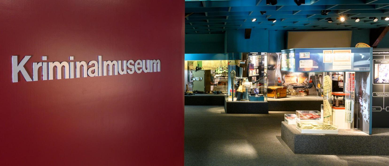 Wand mit der Aufschrift Kriminalmuseum, dahinter Vitrinen mit Exponaten.