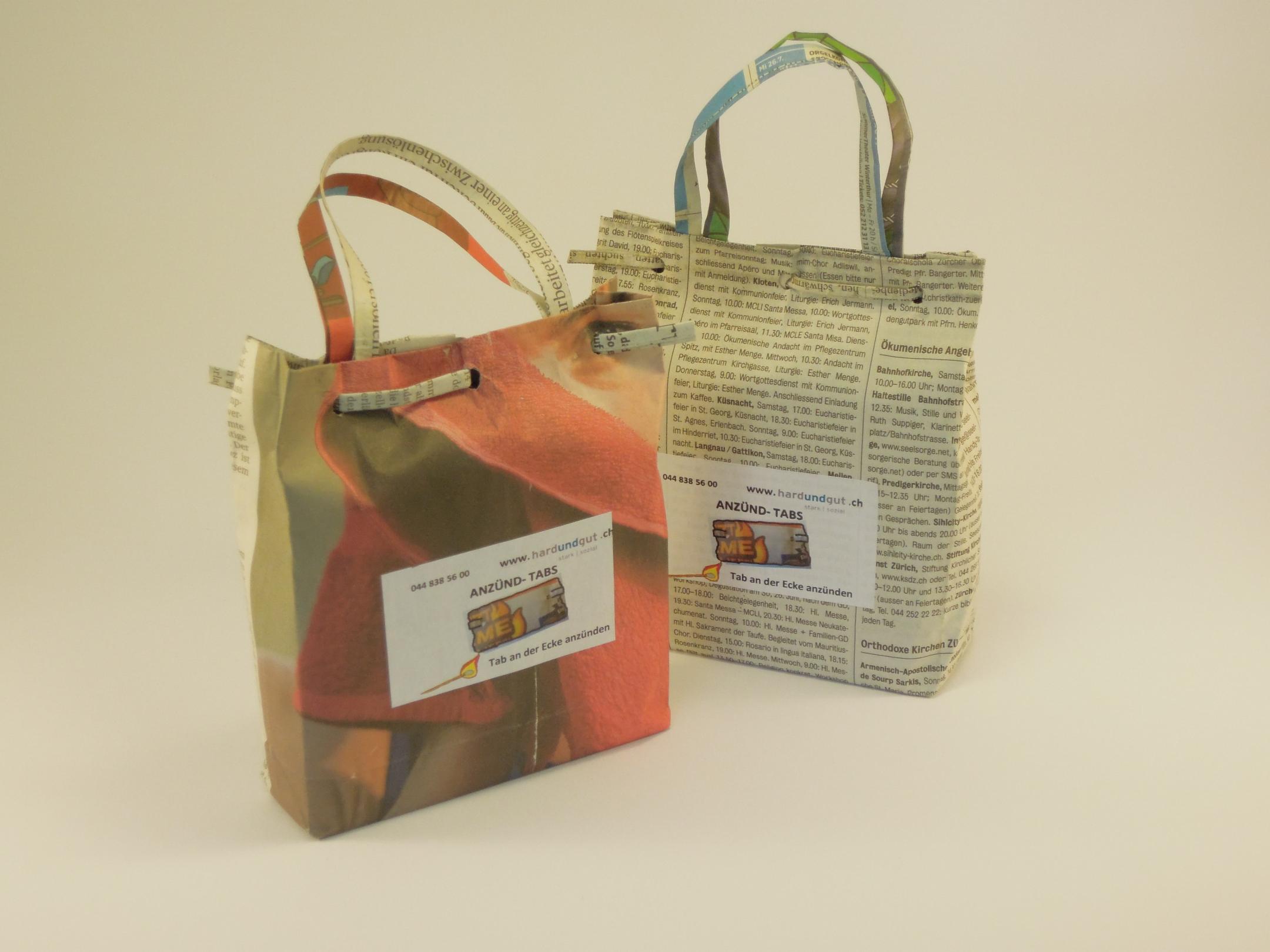 Auf dem Bild sind zwei Geschenktaschen aus Zeitungspapier zu sehen. Der Hintergrund ist neutral.