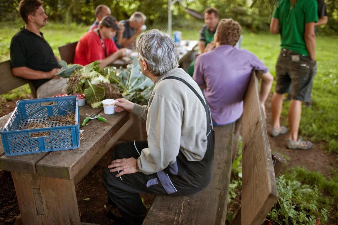 Bewohnerinnen und Bewohner an einem Tisch, auf dem sich frisch geerntetes Gemüse befindet.