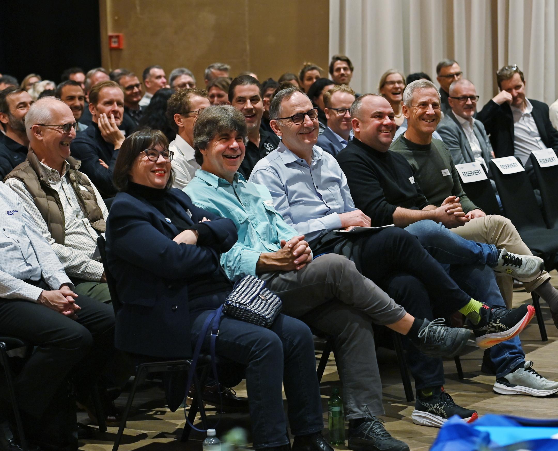 Teilnehmende des Forums Sportkanton Zürich sitzen auf Stühlen in Konzertbestulung, alle lachen