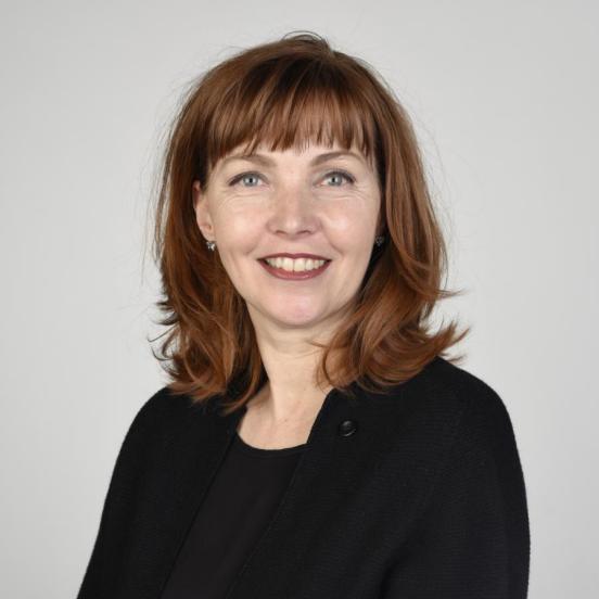 Porträt von Isabelle Sterchi Pelizzari. Sie lächelt, hat schulterlange, rotbraune Haare, einen Pony und grau-blaue Augen. Sie befindet sich vor einem grauem Hintergrund und trägt ein schwarzes Oberteil.