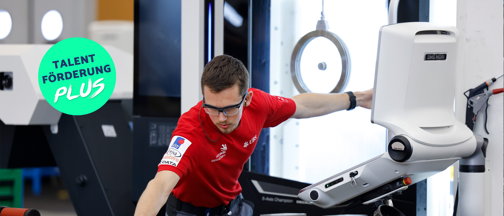 Junger Mann in rotem T-Shirt mit Brille arbeitet an einer grauen Maschine, links eingeblendeter Text «TALENTFÖRDERUNG PLUS».