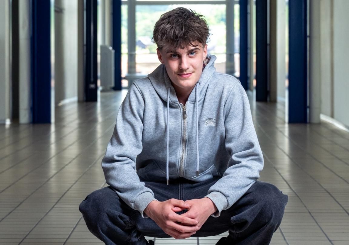  Lernender mit grauem Hoodie in der Hocke im Gang seiner Berufsfachschule.