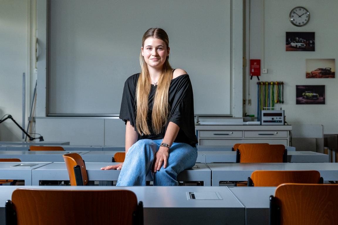 Junge Frau mit langen Haaren sitzt auf einem Pult im Klassenzimmer. 