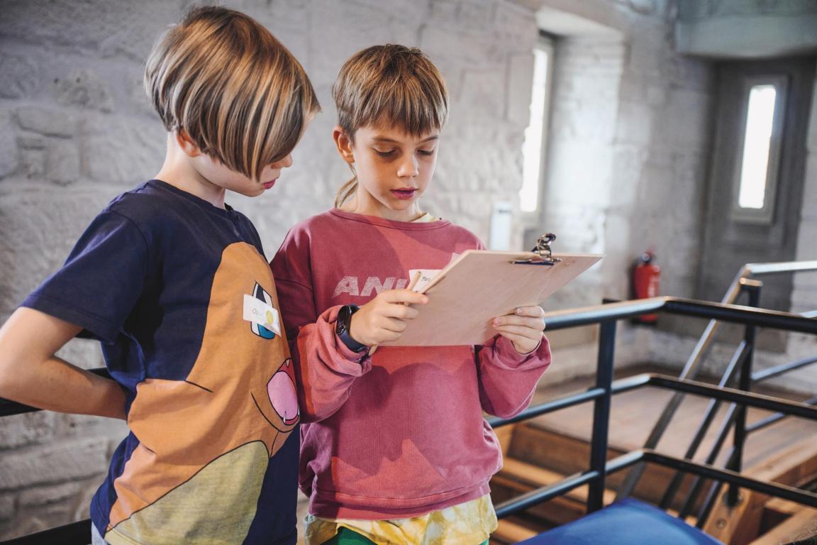 Zwei Schüler lesen gemeinsam etwas von einem Klemmbrett ab. 