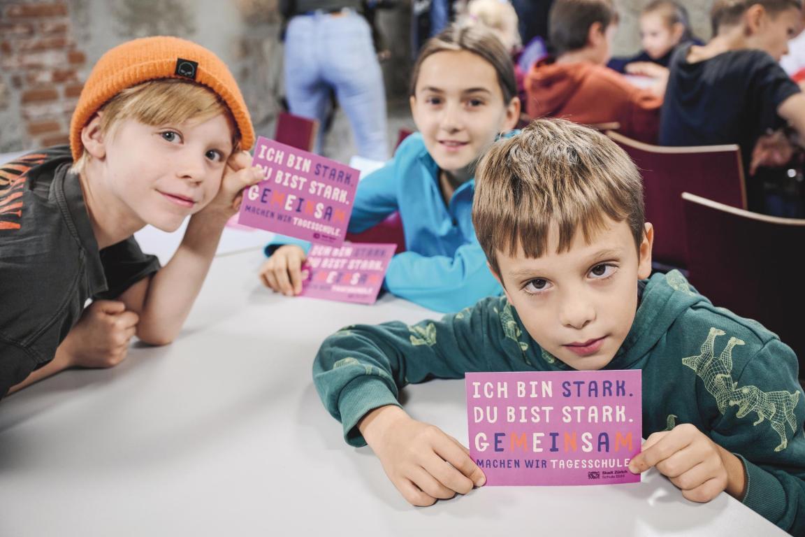 Drei Kinder schauen in die Kamera und halten violette Karten in den Händen. 