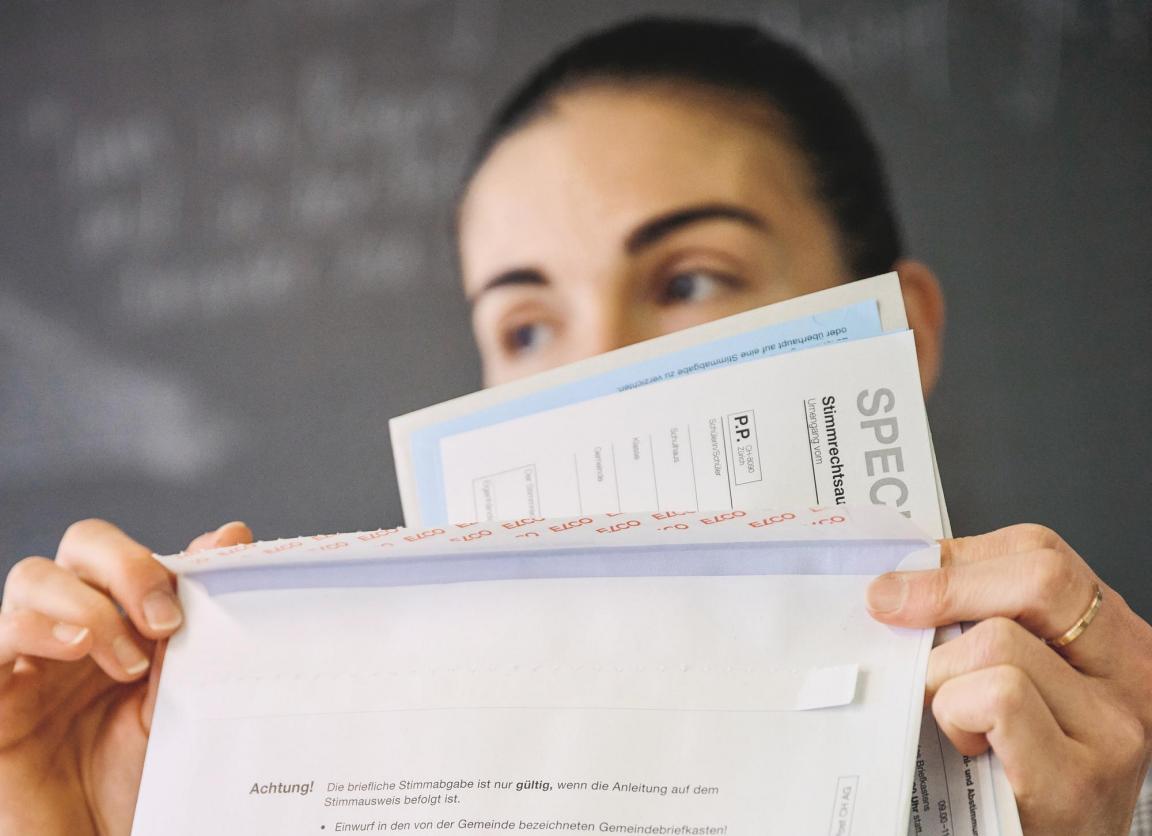 Eine Lehrerin hebt das Abstimmungscouvert und dessen Inhalt hoch, um es der Klasse zu zeigen.