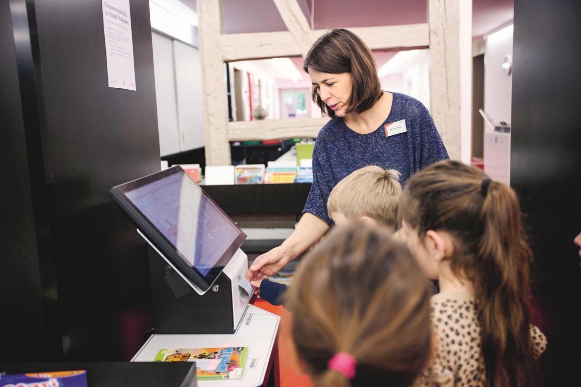 Die Bibliothekrain unterstützt die Kinder am Ausleihautomaten der Bibliothek.