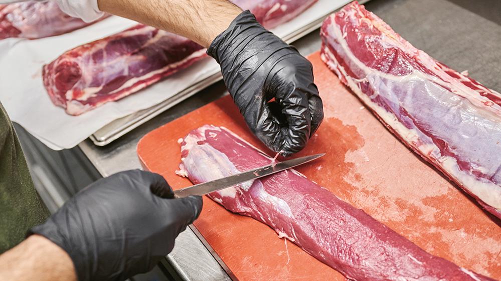 Eine Person, von der man nur die Hände sieht, verarbeitet Fleischstücke. 